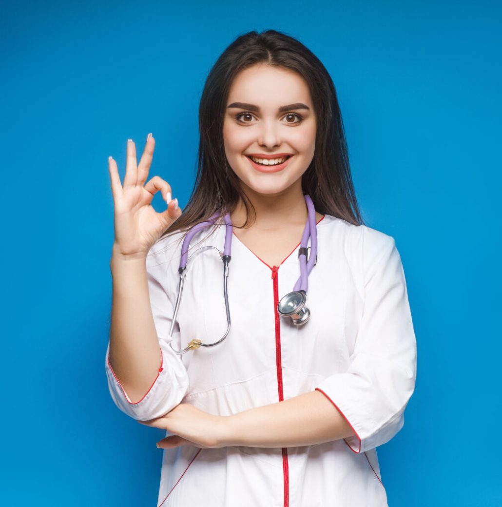 Photo of young female doctor make okaysign, over blue background.